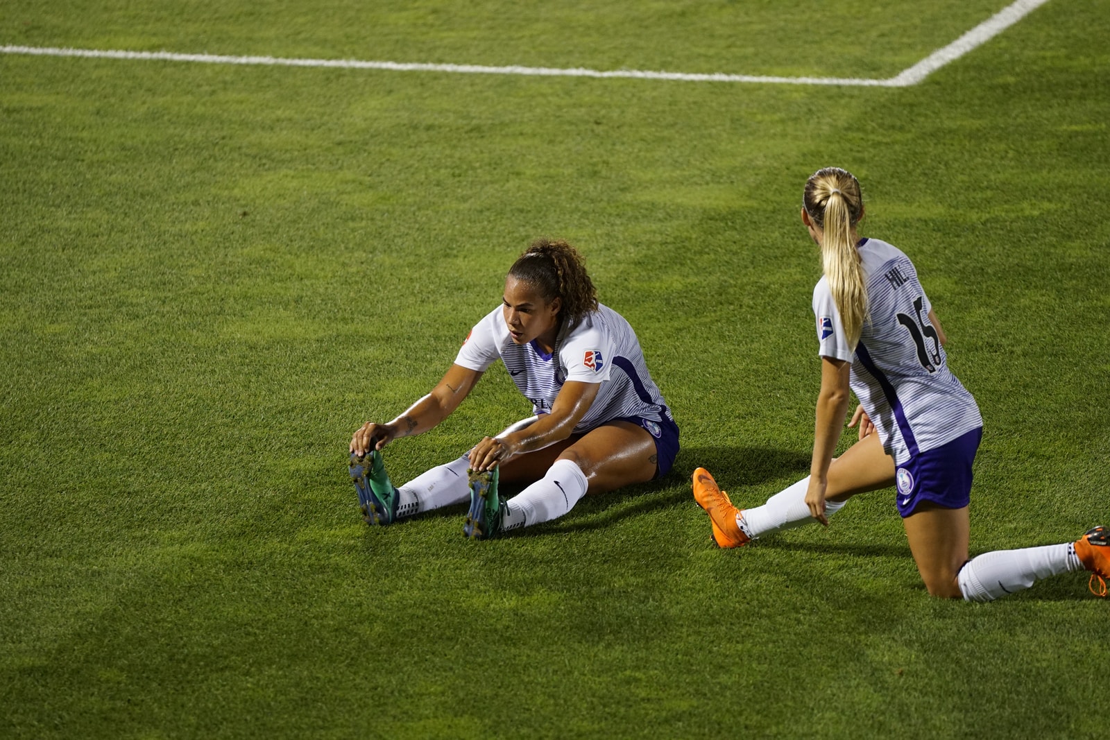 two women soccer players stretching legs on lawn